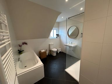 A bathroom with bathtub toilet sink round mirror and glass shower at South Bay House in Scarborough