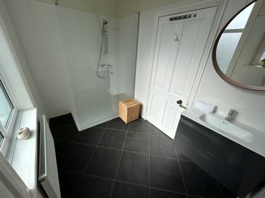 A bathroom with a walk-in shower a white door a black vanity with a sink and a round mirror at South Bay House in Scarborough
