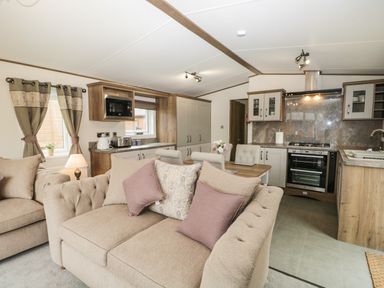 A living area with beige sofas and pillows next to a kitchen with wooden cabinets and appliances at Ashton Lodge - Sherwood 4 in South Lakeland Leisure Village