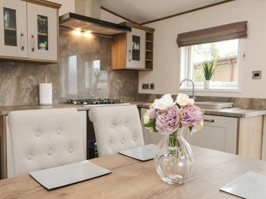 A kitchen and dining area with a gas stove flowers in a glass vase on the table and a window with a plant at Ashton Lodge - Sherwood 4 in South Lakeland Leisure Village