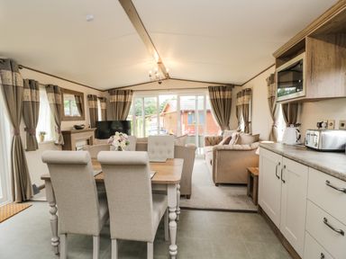 An open living room and kitchen with a dining table, chairs, sofas, curtains, and kitchen appliances at Ashton Lodge - Sherwood 4 in South Lakeland Leisure Village