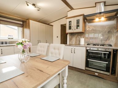 A kitchen with a wooden table and flowers in a vase with beige chairs and a stove oven at Ashton Lodge - Sherwood 4 in South Lakeland Leisure Village