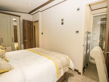 A bedroom with a bed and checked bedding next to a wardrobe and an open door leading to a bathroom at Ashton Lodge - Sherwood 4 in South Lakeland Leisure Village