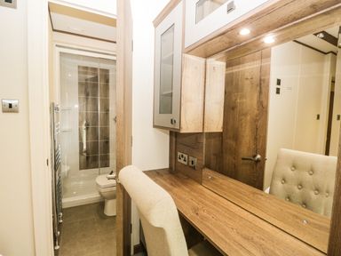 A bathroom with a shower and toilet next to a wooden dressing table with a chair at Ashton Lodge - Sherwood 4 in South Lakeland Leisure Village