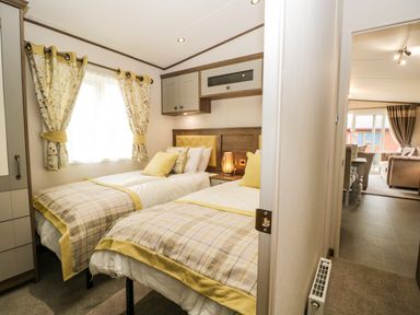 A bedroom with twin beds and patterned curtains connected to a living area at Ashton Lodge - Sherwood 4 in South Lakeland Leisure Village