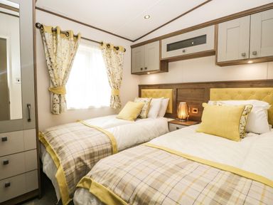 A bedroom with two single beds floral curtains and built in cabinets at Ashton Lodge - Sherwood 4 South Lakeland Leisure Village