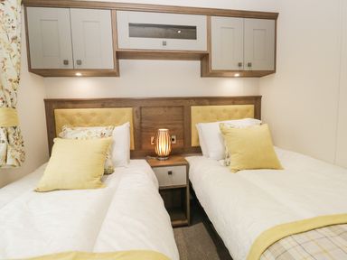A bedroom with two single beds with yellow cushions and a lamp on a bedside table at Ashton Lodge - Sherwood 4 in South Lakeland Leisure Village
