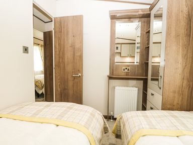 A bedroom with two single beds a wooden wardrobe a dressing table with mirror and an open door showing another room at Ashton Lodge - Sherwood 4 in South Lakeland Leisure Village