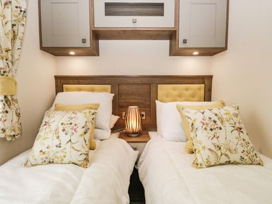 Two single beds with floral pillows and a wooden headboard with yellow padding at Ashton Lodge - Sherwood 4 at South Lakeland Leisure Village