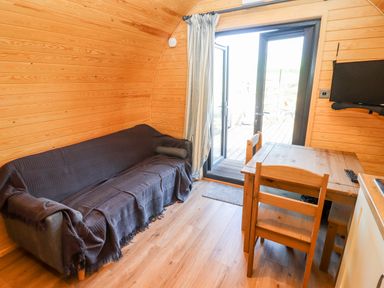 A wooden interior with a covered sofa a wooden table and chairs and a wall-mounted TV at Goose Pod Near Clifton Upon Teme