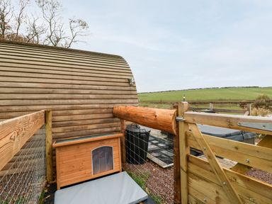 An outdoor fenced area with a wooden dog house a wooden gate a hot tub and a grassy field at Goose Pod Near Clifton Upon Teme