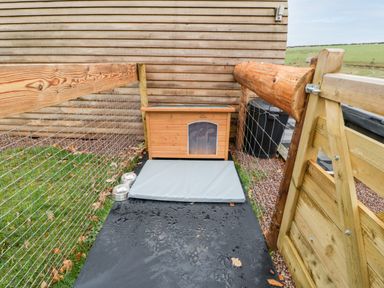 An outdoor enclosed pet area with a wooden dog house a gray mat and two metal bowls at Goose Pod Near Clifton Upon Teme
