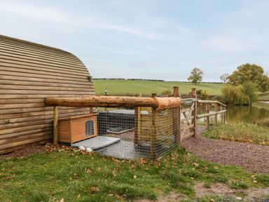 An outdoor area with a wooden fence and a small wooden shelter next to a pond at Goose Pod Near Clifton Upon Teme