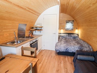 A small wooden room with a kitchen area dining table bed and sofa at Gander Pod Near Clifton Upon Teme