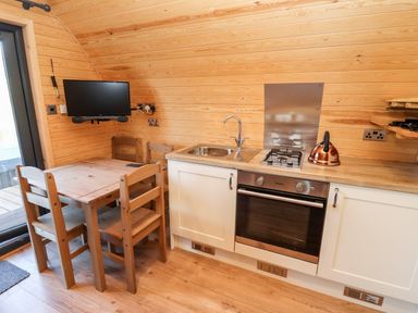 A small kitchen with wooden dining table and chairs a sink stovetop and oven at Gander Pod Near Clifton Upon Teme