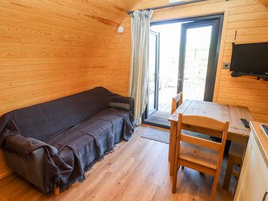A small wooden room with a covered sofa a wooden table and chairs a wall-mounted tv and glass doors leading outside at Gander Pod Near Clifton Upon Teme