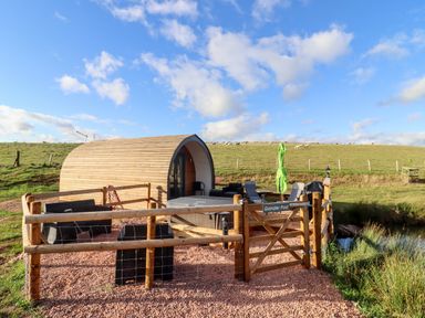 A small wooden pod with outdoor seating and a fenced area in a grassy field at Gander Pod Near Clifton Upon Teme