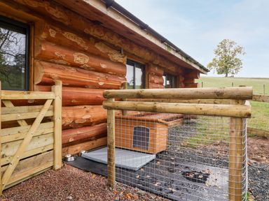 An outdoor area with a wooden dog house fenced with wire mesh near a log cabin at Cedar Cabin Near Clifton Upon Teme