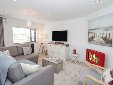A living room with grey sofas a wooden chest coffee table a red fireplace and a TV on a white cabinet at Cove House in Kinmel Bay