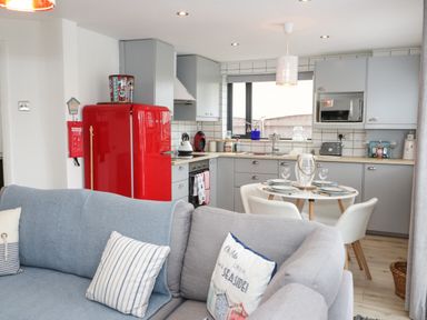 A kitchen with grey cabinets a red refrigerator and a dining table set for four at Cove House in Kinmel Bay