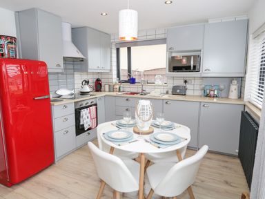 A kitchen with grey cabinets a red fridge a round table set for four and a window at Cove House in Kinmel Bay