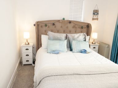 A bedroom with a bed with pillows and stuffed toys with two bedside tables with lamps at Cove House in Kinmel Bay