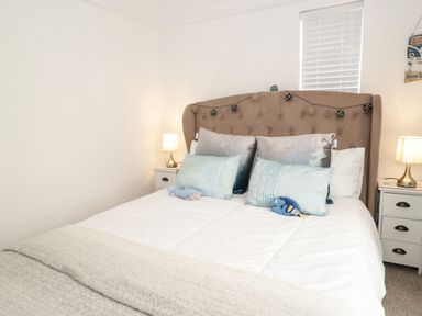 A bedroom with a bed with pillows and stuffed toys and nightstands with lamps at Cove House in Kinmel Bay