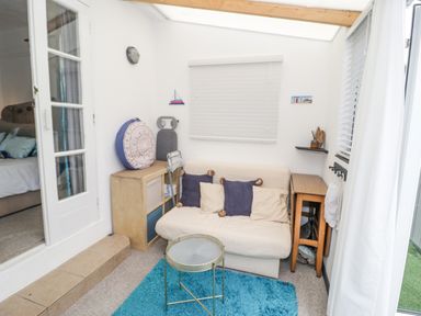 A small sitting area with a beige sofa with cushions a blue rug a round metal table wooden storage units and a window with blinds at Cove House in Kinmel Bay