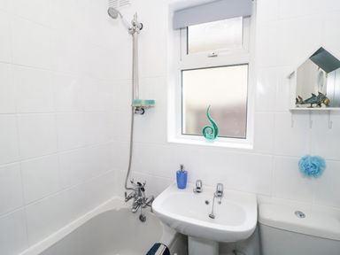 A bathroom with a bathtub shower, sink, window, and toilet at Cove House Kinmel Bay