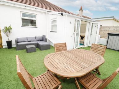 An outdoor patio with wooden table and chairs and a gray sectional sofa at Cove House in Kinmel Bay