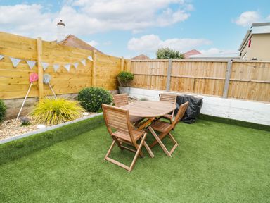 A backyard with wooden table and chairs on artificial grass with wooden fences around at Cove House in Kinmel Bay