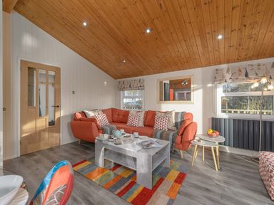 A living room with an orange sofa cushions a coffee table and a multicolored rug at Oaks One Swarland near Felton