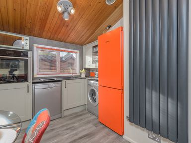 A kitchen with an orange refrigerator dishwasher washing machine window and gray vertical radiator at Oaks One Swarland near Felton
