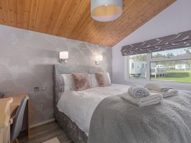 A bedroom with a bed towels on it a desk and chair next to a window showing caravans outside at Oaks One Swarland near Felton