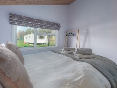 A bedroom with a bed and pillows towels on the bed a window with a view of a trailer and a clothes rack with hangers at Oaks One Swarland near Felton