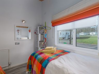 A bedroom with a single bed and colorful blanket next to a window showing mobile homes outside at Oaks One Swarland near Felton