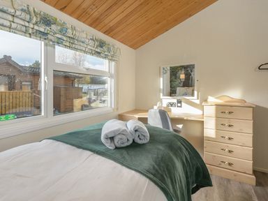 A bedroom with a bed with towels on it a window with floral blinds a desk with a chair a mirror and a chest of drawers at Oaks One Swarland near Felton