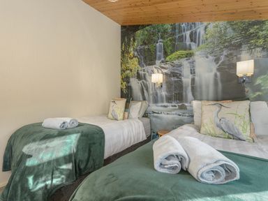 A bedroom with two single beds with green blankets and rolled towels with a waterfall mural on the wall at Oaks One Swarland near Felton