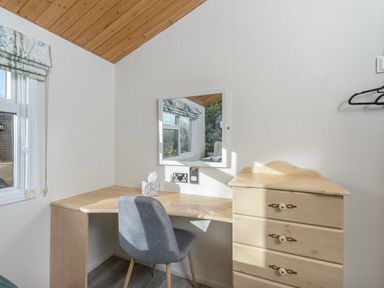 A corner desk with tissue box and mirror above and a grey chair next to a wooden chest of drawers in a room at Oaks One Swarland near Felton