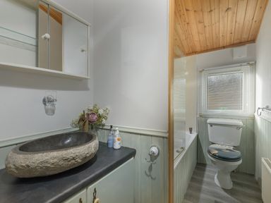 A bathroom with a stone sink a bathtub and a toilet under a window at Oaks One Swarland near Felton