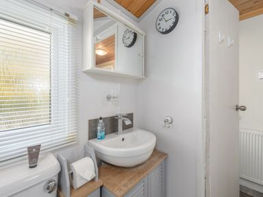 A bathroom with a sink cabinet mirror clock and toilet near a window at Oaks One Swarland near Felton