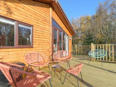 A wooden deck with outdoor chairs and a small table outside a cabin at Oaks One Swarland near Felton