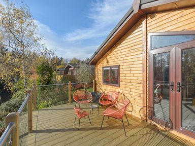 An outdoor wooden deck with four orange chairs and a small table next to a wooden cabin with glass doors and windows at Oaks One Swarland near Felton