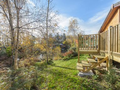 A wooden deck with chair and stairs leading to a garden with trees and grassy area at Oaks One Swarland near Felton