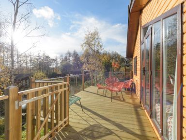 A wooden deck with chairs and glass doors overlooking trees at Oaks One Swarland near Felton