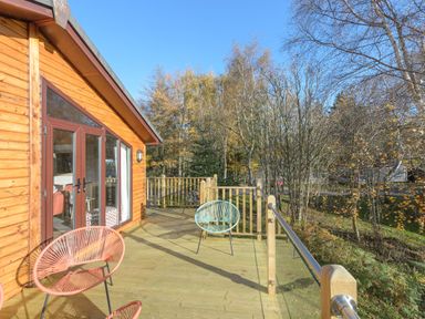 A wooden deck with three chairs outside a cabin surrounded by trees at Oaks One Swarland near Felton