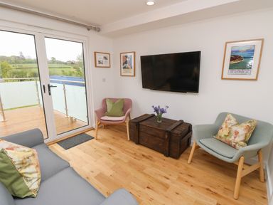 A living room with a gray sofa and two armchairs facing a wall-mounted TV and a wooden chest at Pinot in Seaview