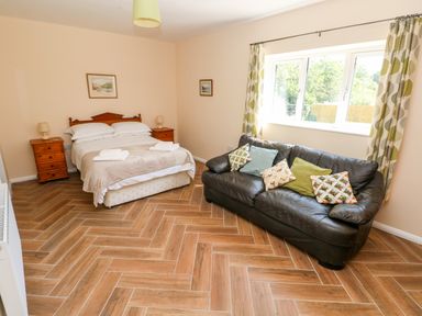 A bedroom with a double bed flanked by wooden bedside tables and a black sofa with cushions near a window at 1 The Warren in Robeston Wathen near Narberth