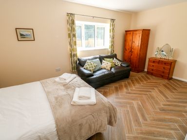 A bedroom with a bed, sofa with cushions, wooden wardrobe, and dresser with mirror at 1 The Warren Robeston Wathen near Narberth