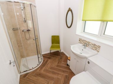 A bathroom with a glass shower enclosure a green chair a sink with cabinetry and an oval mirror at 1 The Warren Robeston Wathen near Narberth